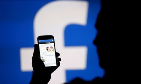 A man is silhouetted against a video screen with an Facebook logo