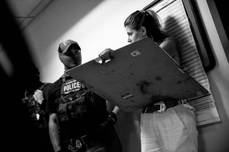 A woman holds an easel as she draws masked agents waiting in a hallway