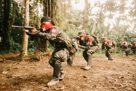 Fighters in combat gear and with red and black bandanas covering their noses and mouths crouch and point their rifles