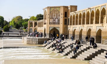 People sitting on steps leading down to a river in Isfahan