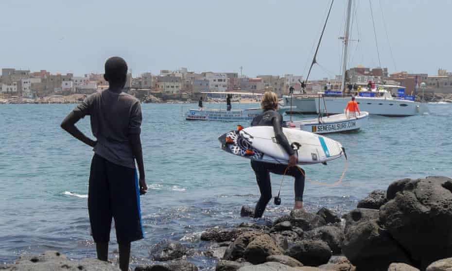 A local boy watches South African surfer Beyrick De Vries head out towards the surf at Ngor, Senegal