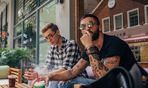 Two male friends drinking takeaway coffee and smoking cigarette.