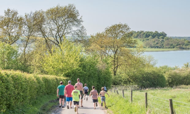 A group of three men walk down a road on a hot day to Rutland Water, England, as four children run past them