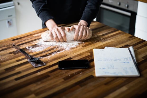 A woman kneading sourdough with a phone and a notebook