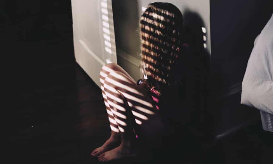 Girl sitting by window casting shadows of blinds