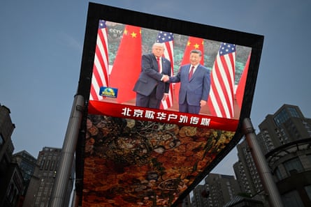 a screen displays Donald Trump and Xi Jinping shaking hands