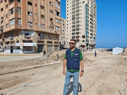 Man in blue WFP vest standing on rubble-strewn street and damaged high-rises
