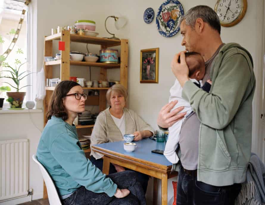 Marc Wilson holds his baby son, at the kitchen table with his wife, Anna, and her mother, who was visiting from Ukraine when the war started. They await news of family members’ UK visa status and from Anna’s father who is still trapped in Ukraine.