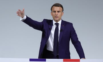 Emmanuel Macron speaking at podium with hand raised.