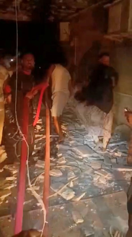 Men seen inside a dark room with debris strewn on the floor.