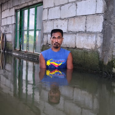 A man stands chest-deep in flood water next to a brick wall