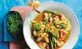 Topview of a stirfry of asparagus, prawns and macadamia in a bowl, with a side of rice.