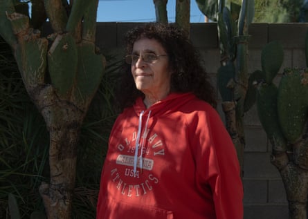 A woman in a red hoodie stands under the shade of a tree