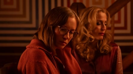 Two tousled women look off camera in a room with dark red and brown lighting.