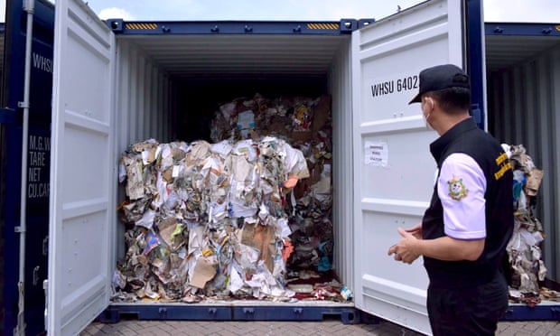 A policeman looks at a container full of bales of plastic waste