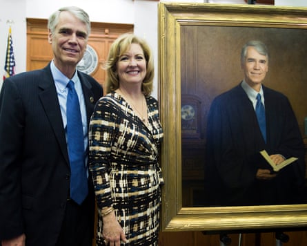 A judge and his wife smile by a portrait of the man