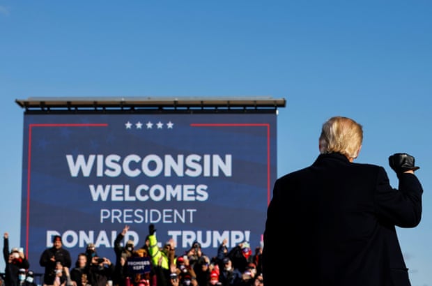 Donald Trump is seen from behind as he raises a fist to a crowd. A sign behind the crows reads 'Wisconsin welcomes president Donald Trump!'