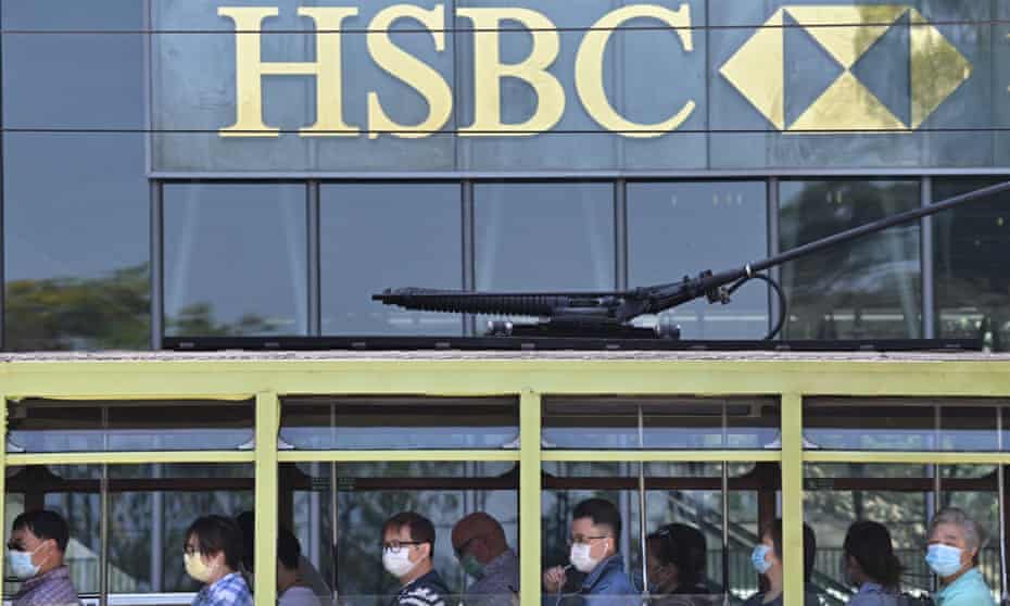 Commuters wearing face masks travel on a tram past HSBC signage displayed outside the banks local headquarters in Hong Kong
