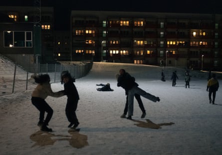 Young people silhouetted, having fun outside in snowy area after dark, with a block of flats behind