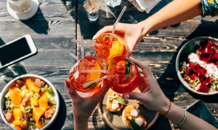 A toast over food of three Aperol spritzs