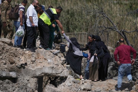 एक आदमी एक महिला को नष्ट हुए पुल के बगल में मलबे पर चढ़ने में मदद करता है।