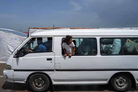A child peeks out of a window of a van packed with their family’s belongings
