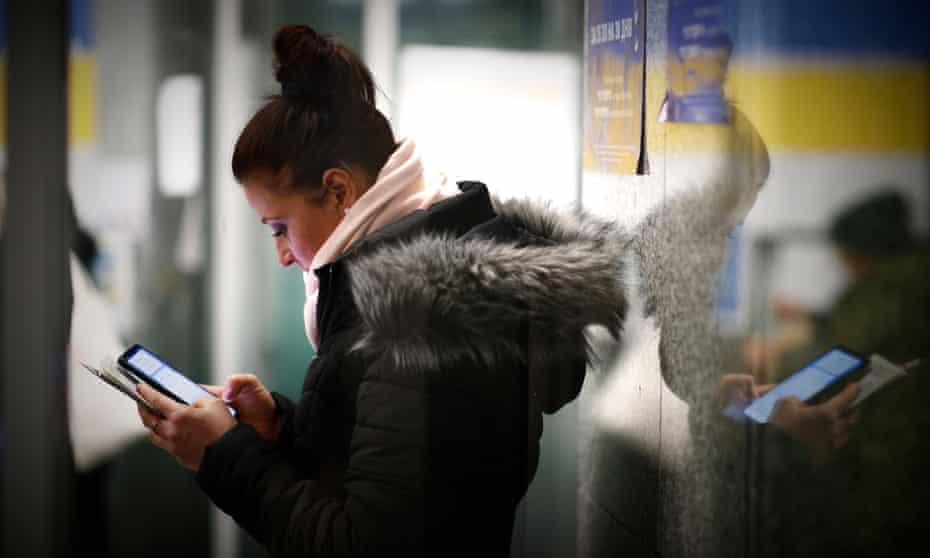 A woman using her mobile phone with a post of a Ukraine flag in background.