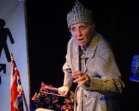 Nichola McAuliffe, in a decorative crown and plaid coat, performs behind a flower-adorned walker