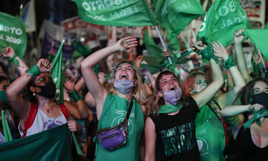 Young women dressed in green and waving banners cheer in the street as the law is passed