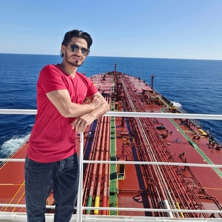 Young South Asian man posing on a walkway above deck of a large tanker ship
