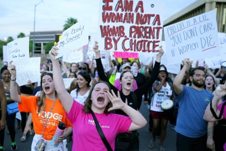 A group of protesters hold signs and shout. The most prominent sign declares 'I am a woman, not a womb. Parent by choice'.