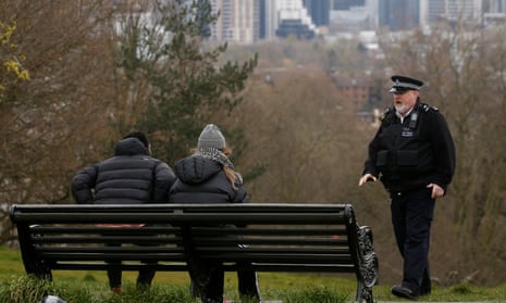 a male police officer talks to a man and a woman on a bench in Greenwich Park, London