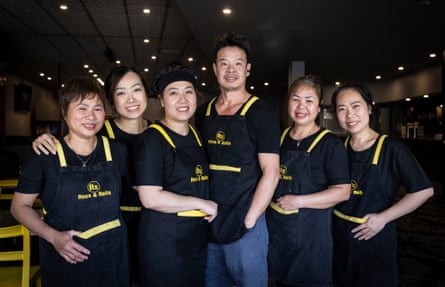 Six staff members of a Vietnamese restaurant in matching black aprons.