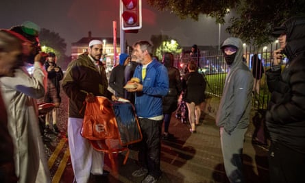 Adam Kelwick holds a large bag while talking to a man holding a burger box and others watch on