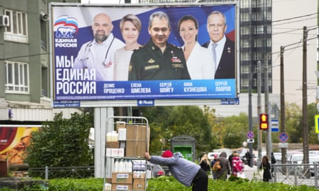 A store worker rolls a cart with groceries past election posters depicting candidates for the State Duma, the lower house of the Russian parliament.