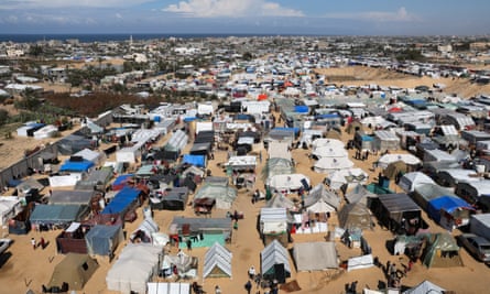 A vast expanse of ground filled with tents. The sea can be seen on the horizon.