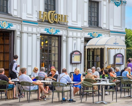 Diners sit at tables outside an ornate restaurant decorated in art nouveau style.