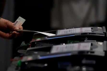 Closeup of a voter with license in hand feeding their paper ballot into a scanner