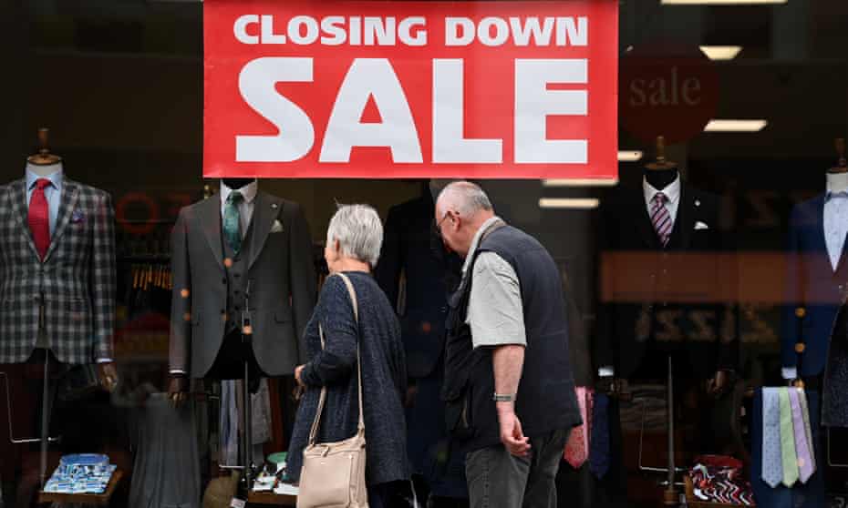 a couple look through the window of a shop with a big 'closing down sale' sign