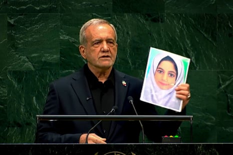 Masoud Pezeshkian speaking on stage holding a picture of a young girl.
