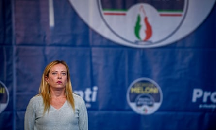 Giorgia Meloni campaigning in Ancora, Italy, with her party’s flag-flame logo, shared with a defunct neo-fascist party, behind her.
