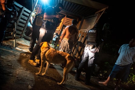 Officers talk to a young man in a dark street with a dog in the foreground