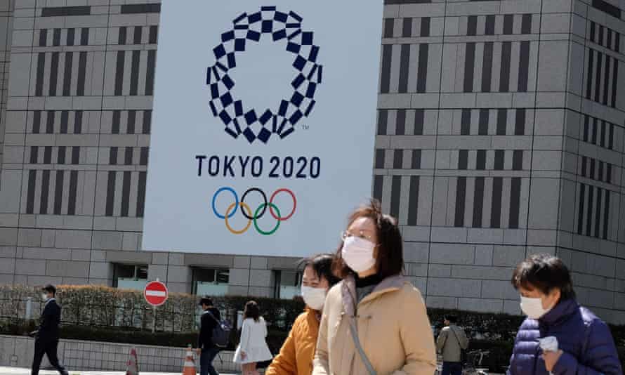 Pedestrians wearing face masks outside the Tokyo Metropolitan Government building, which carries the logo of the 2020 Olympic Games