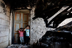 Two children stand next to a burnt car