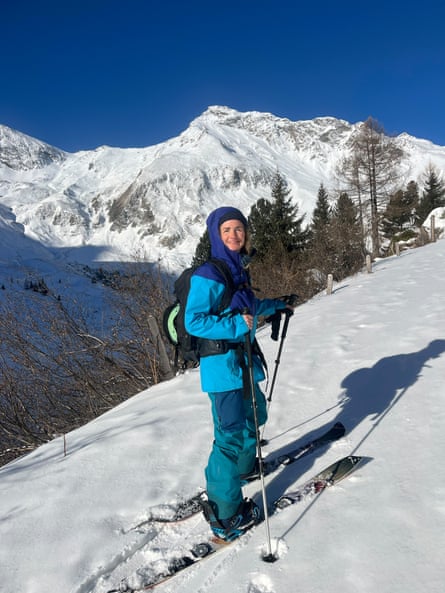 Woman wearing split boards and holding ski poles as she faces upwards on a sunny snowy slope