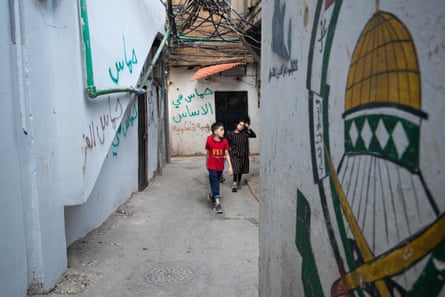 A boy and a girl walk through an alley covered in graffiti. One reads: ‘Hamas’