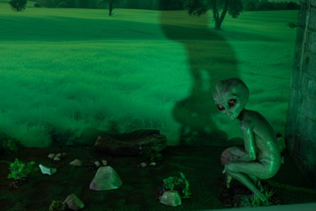 A statue of an alien with big eyes and a crouched body against a green background at the extraterrestrial museum