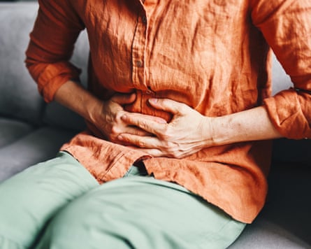 A woman sitting on a sofa and clutching her stomach in pain