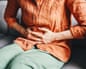 Close-up of a woman holding her abdomen, sitting on a sofa, indicating discomfort or pain in her stomach