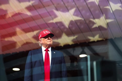 Man in red tie and Maga hat looks out of window at airport